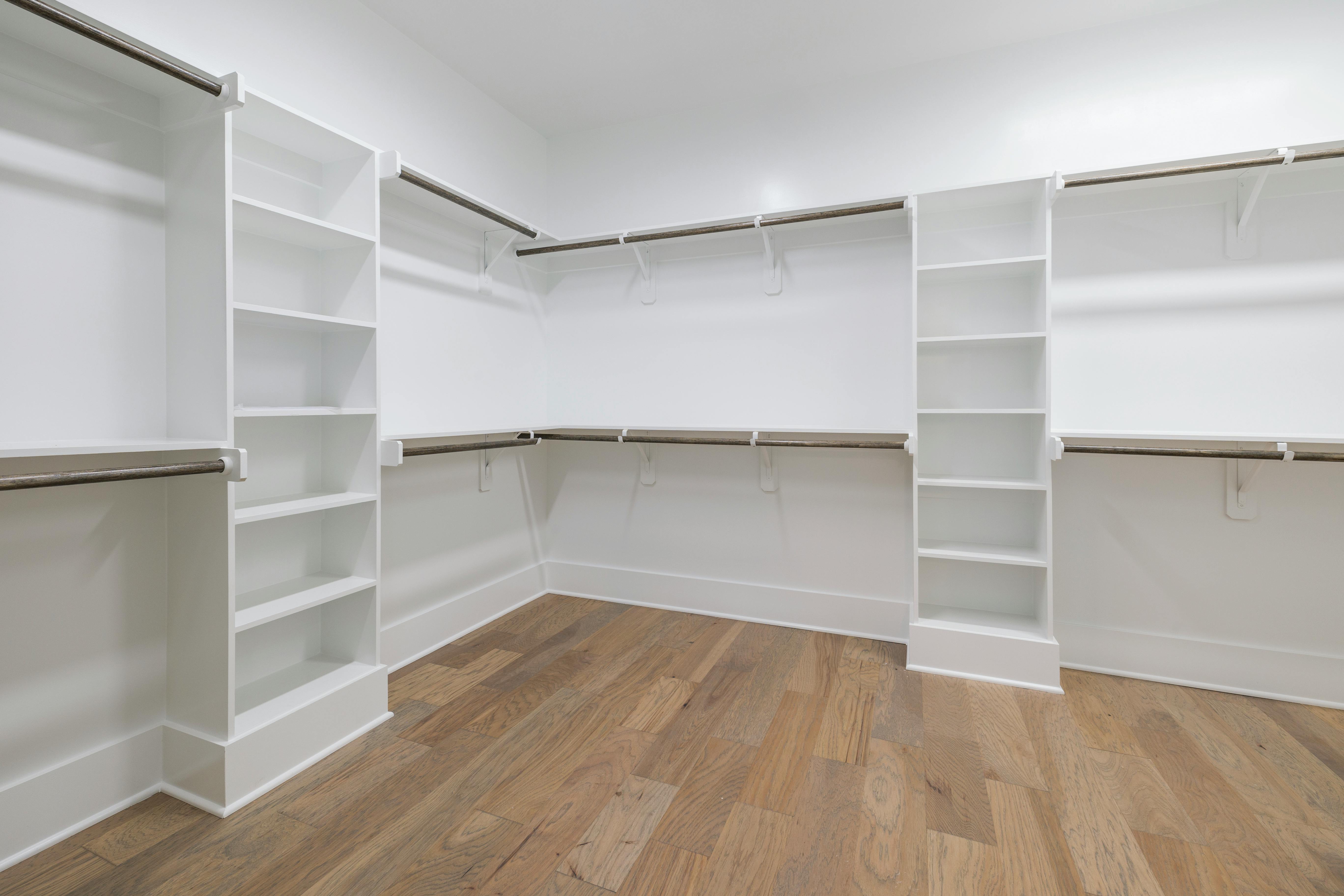 Luxury custom closet with wraparound hanging bars, built-in shelves, hardwood floors, and open layout designed for premium walk-in closet storage.